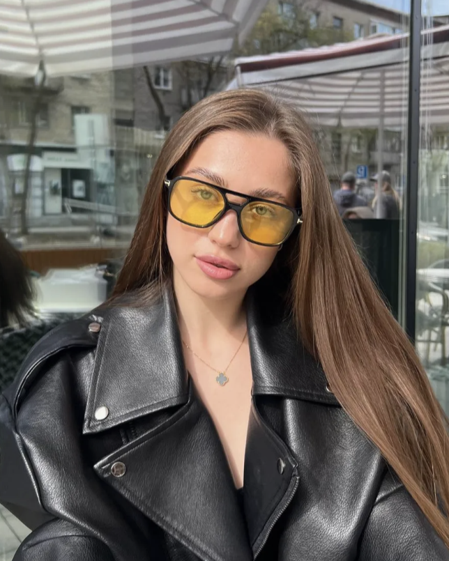 Woman wearing a black leather jacket and yellow-tinted glasses outdoors.