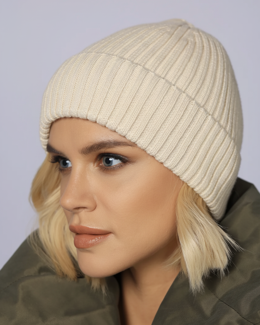 Woman wearing a beige knit beanie against a plain background