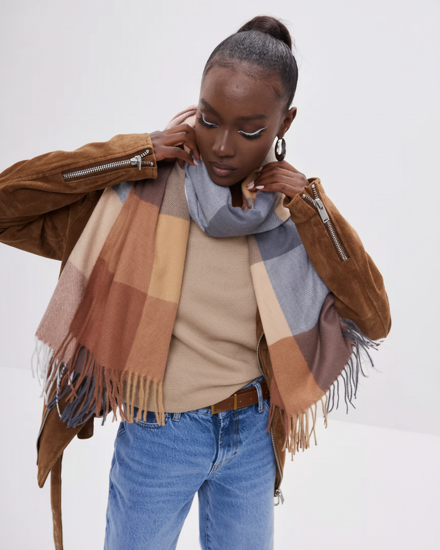 Woman wearing a checkered scarf, brown jacket, beige sweater, and blue jeans on a white background