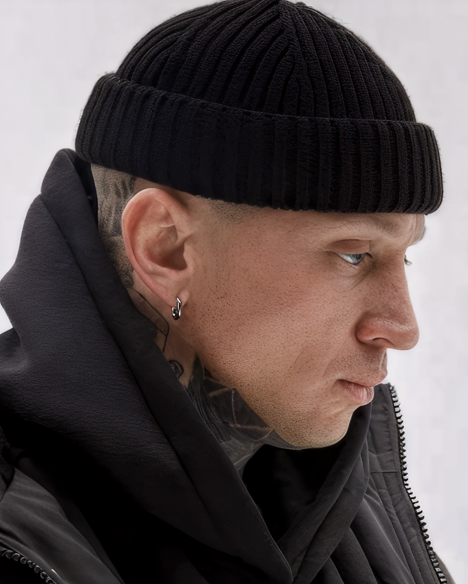 Person wearing a black knit beanie and dark clothing against a white background
