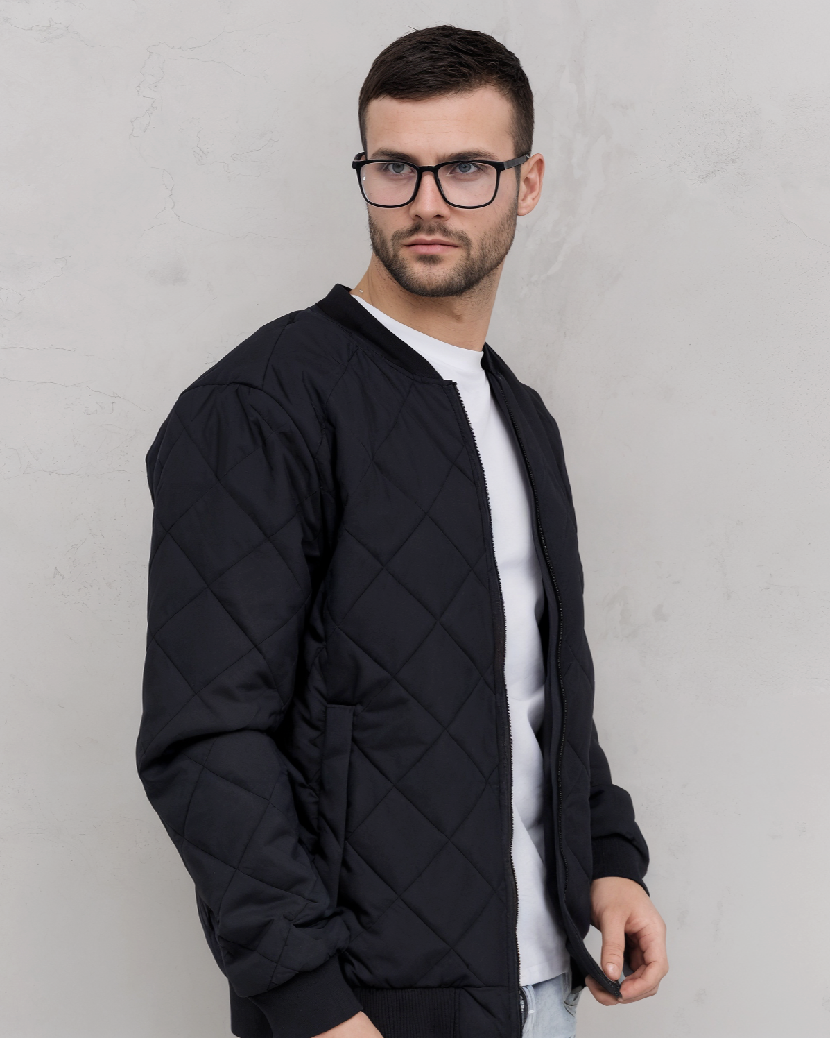 Man wearing a black quilted jacket and glasses against a gray background
