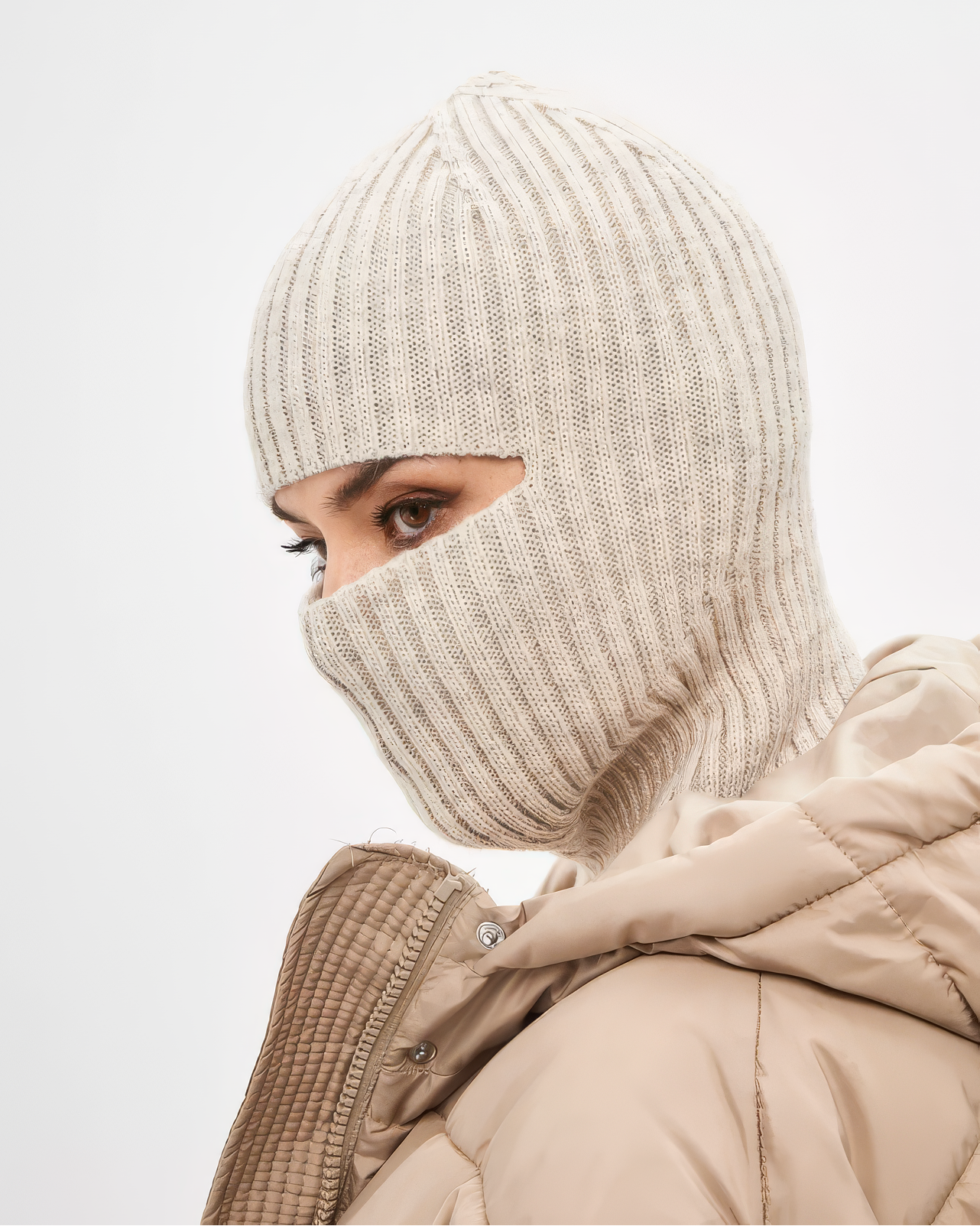 Person wearing a beige knit balaclava and coat on a light gray background
