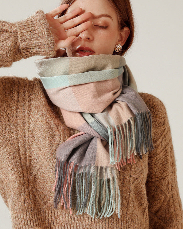 Person wearing a brown sweater and a colorful scarf with fringes on a plain background