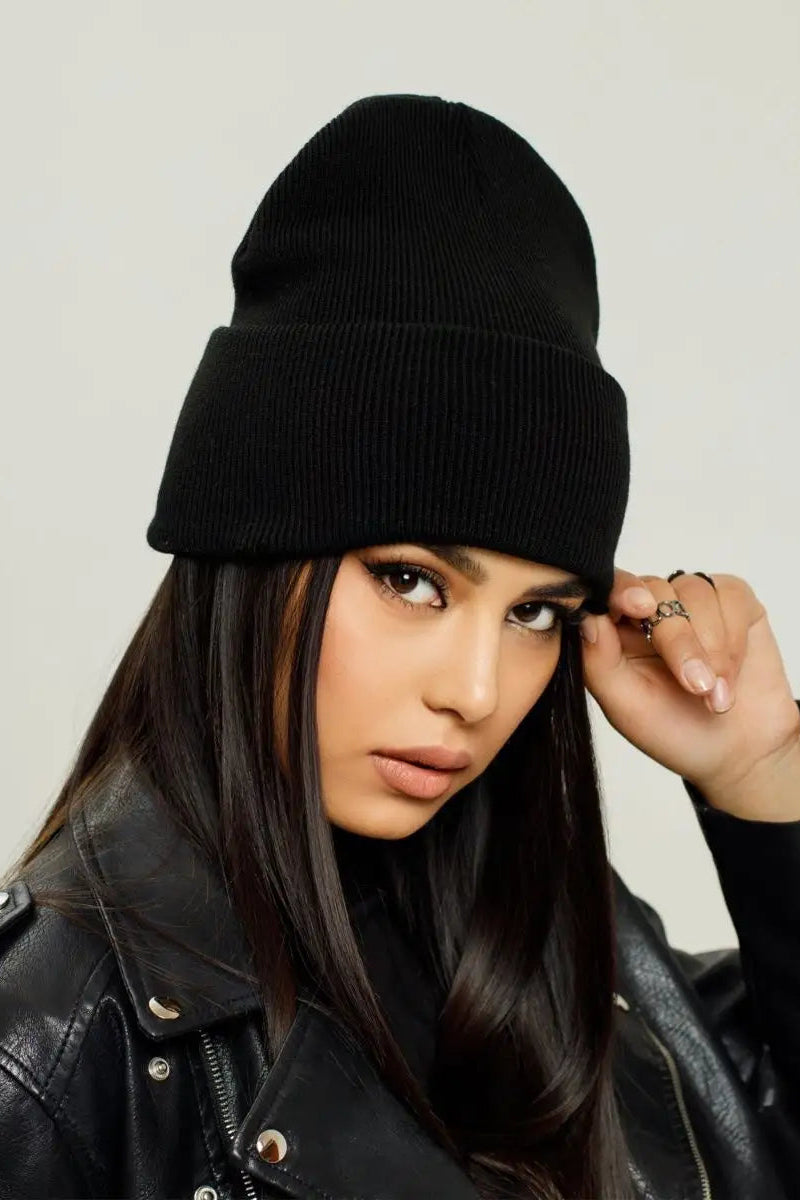 A woman wearing a black ribbed knit cuffed beanie and a black leather jacket, posing against a light gray studio background.