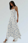 A woman modeling a white spaghetti-strap maxi dress with a blue floral print, styled with white strappy high heels against a plain white studio background.