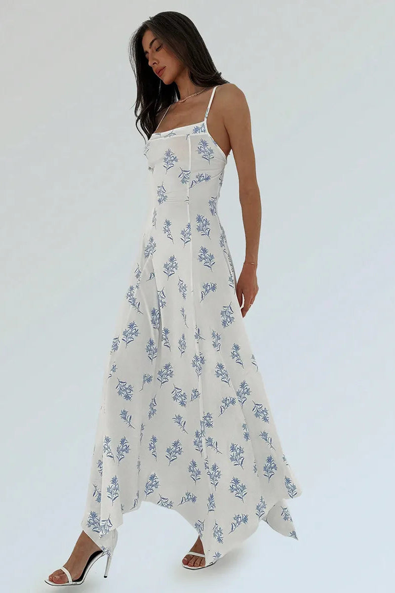 A woman modeling a white spaghetti-strap maxi dress with a blue floral print, styled with white strappy high heels against a plain white studio background.