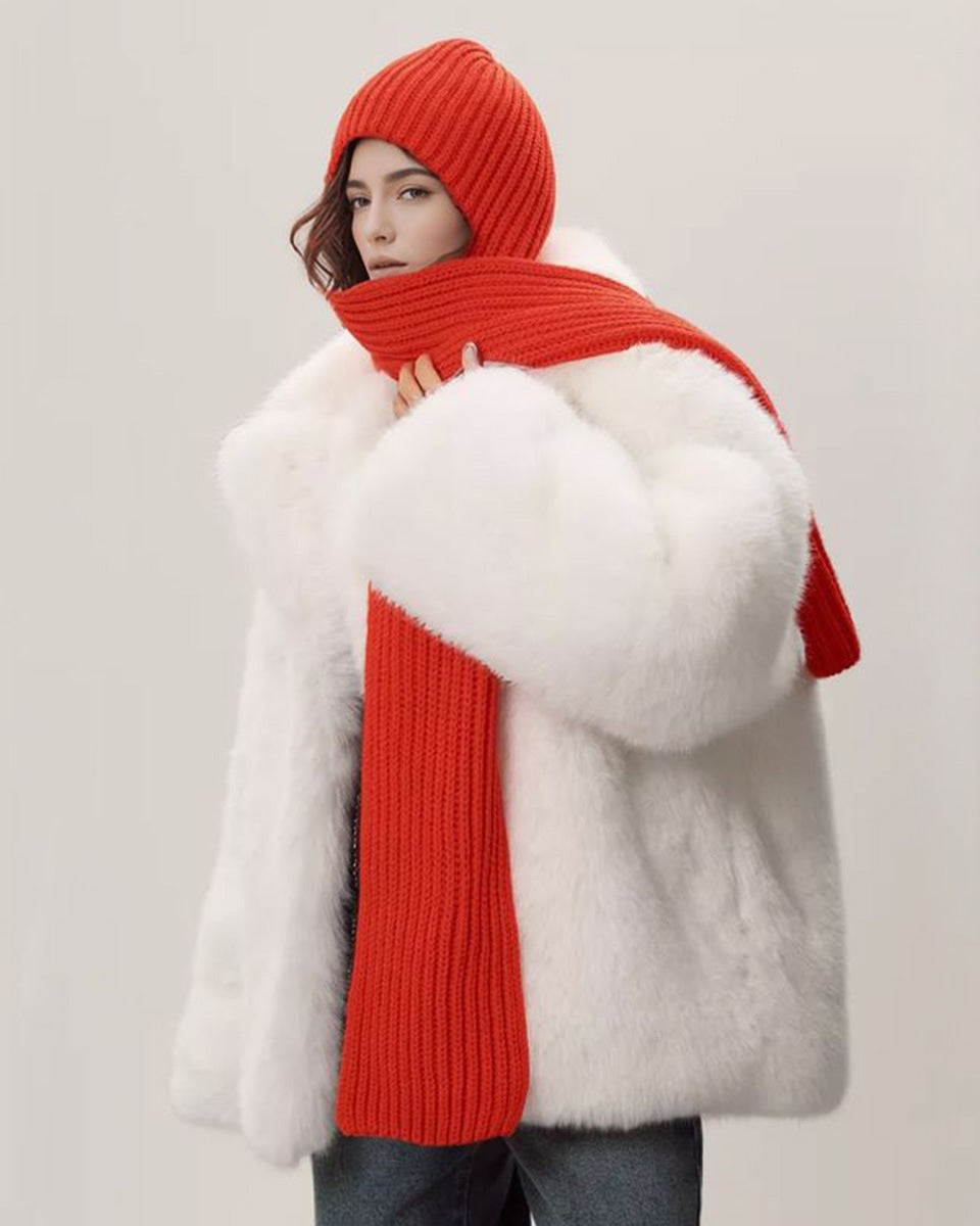 Person wearing a white fur coat and red knit hat and scarf against a plain background