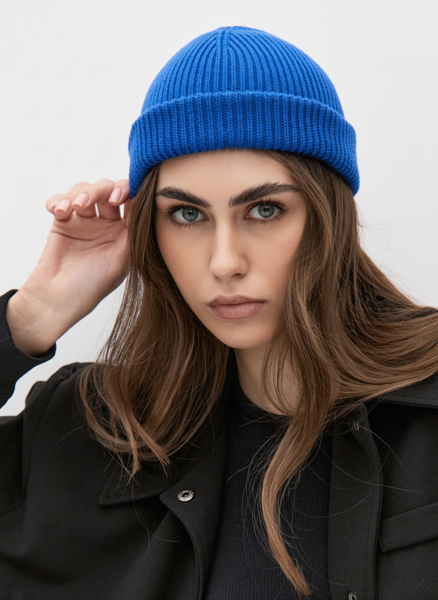 Woman wearing a blue beanie and black coat against a white background