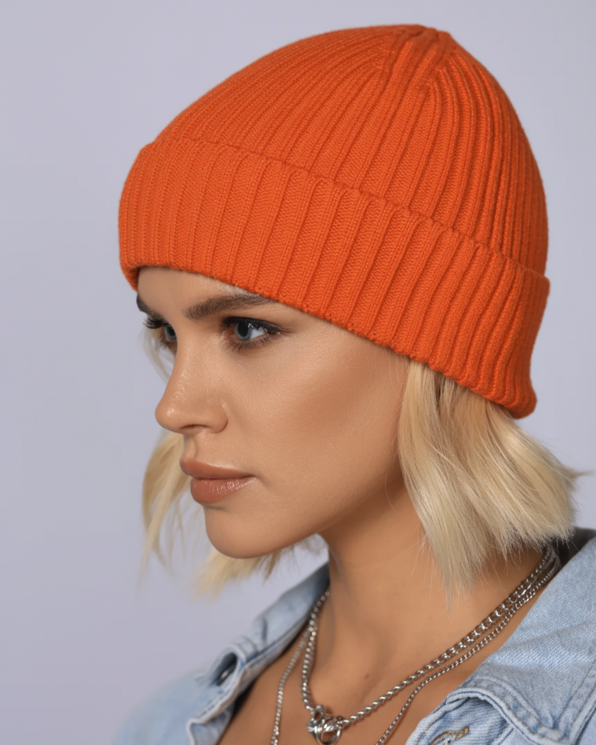 Person wearing an orange knit beanie and denim jacket against a light gray background