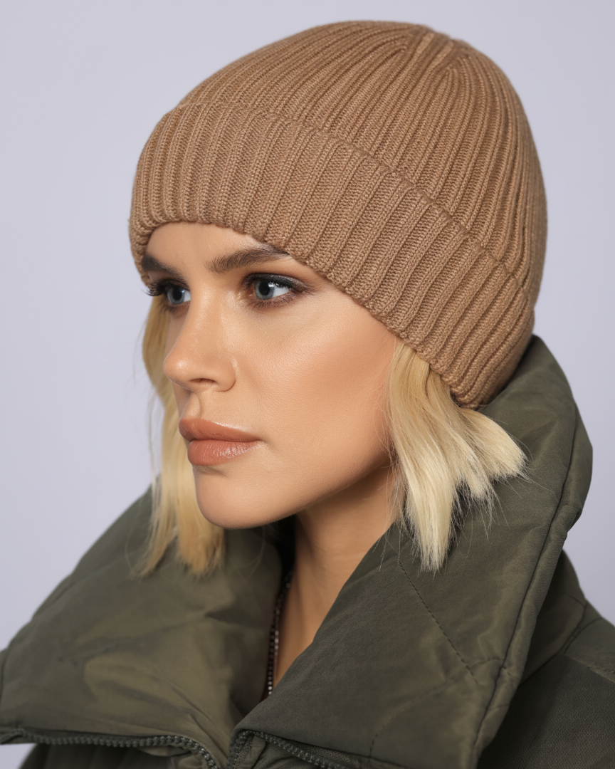 Woman wearing a beige knitted beanie and green coat against a light gray background
