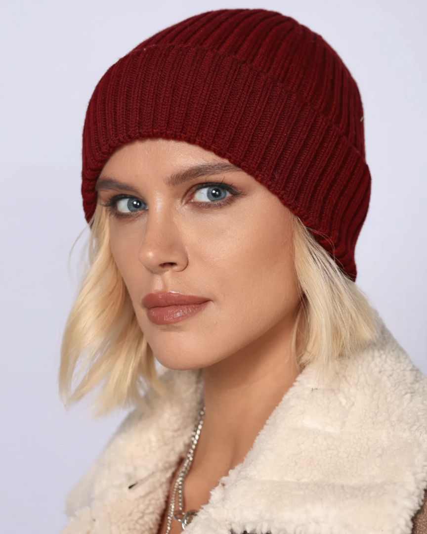Woman wearing a red knit beanie and white fur-lined coat against a light background