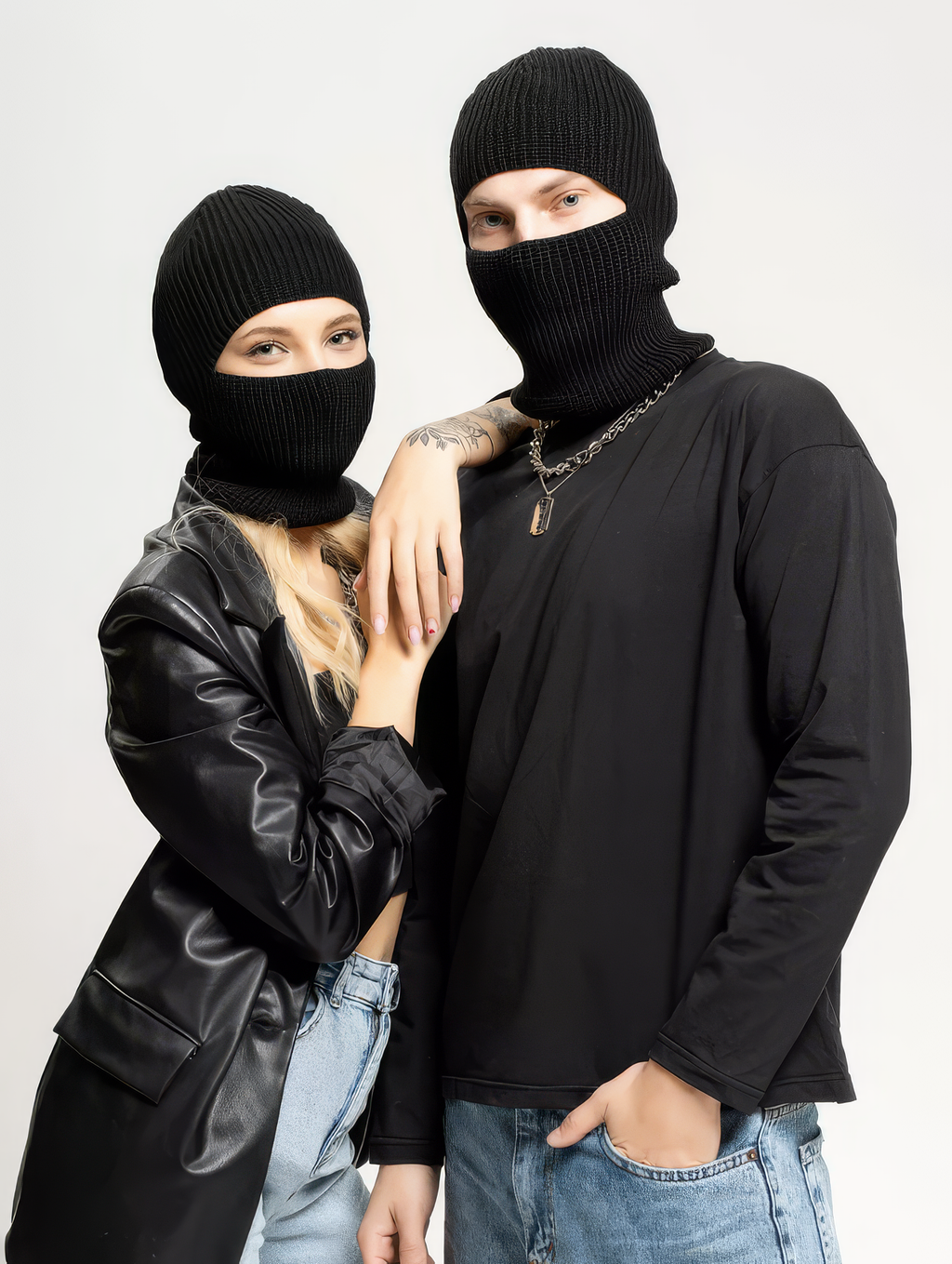 Two people wearing black balaclavas and dark clothing against a light background