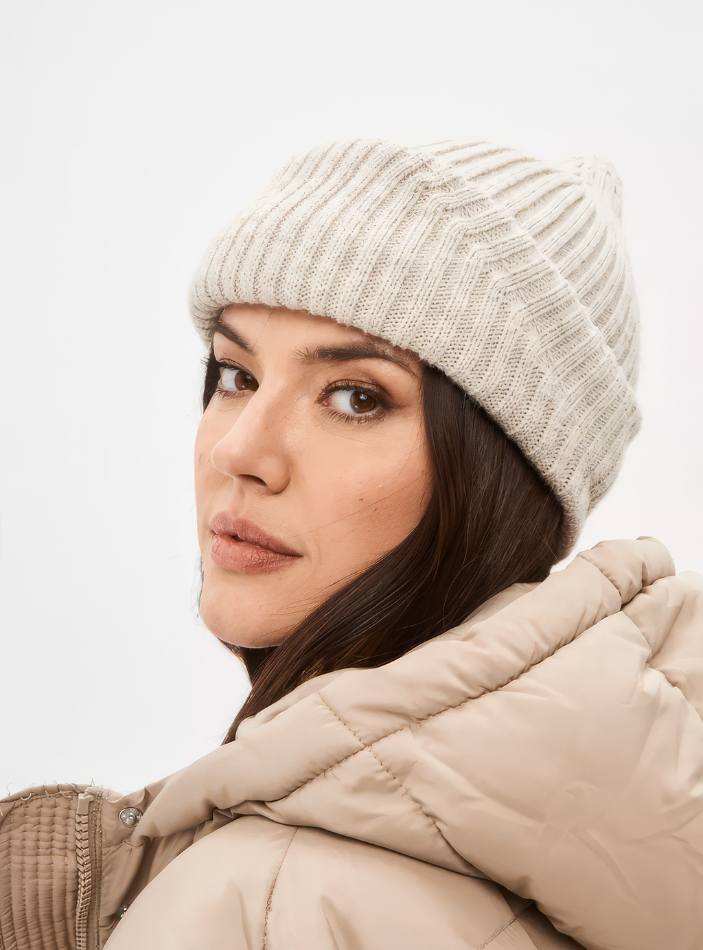 Woman wearing a beige knit beanie and coat on a light gray background