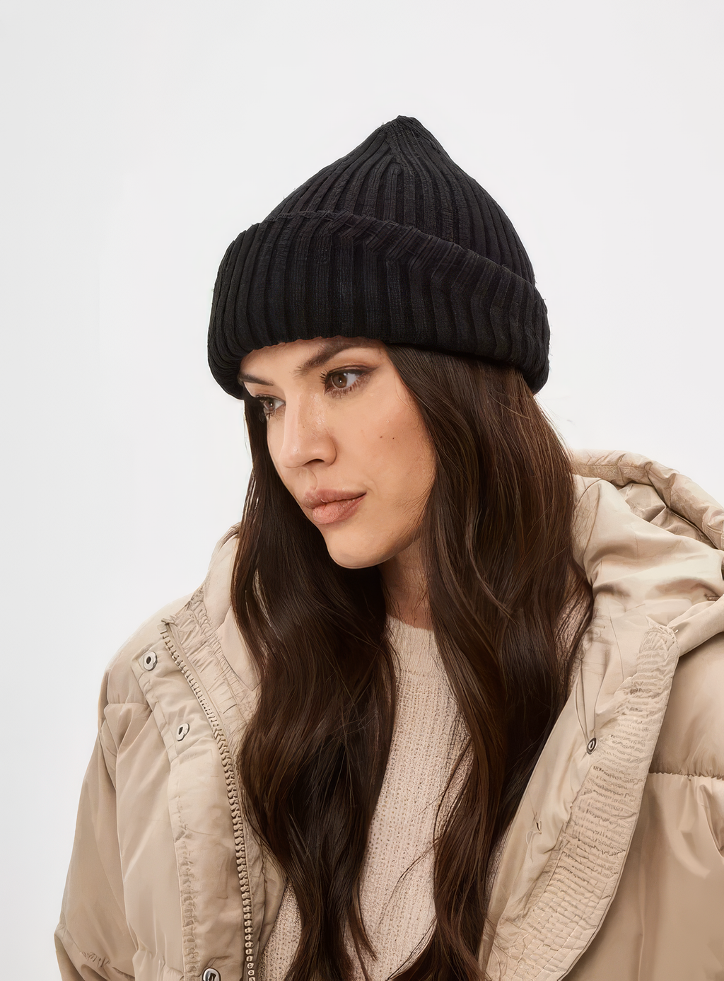 Woman wearing a black knit beanie and beige jacket on a white background