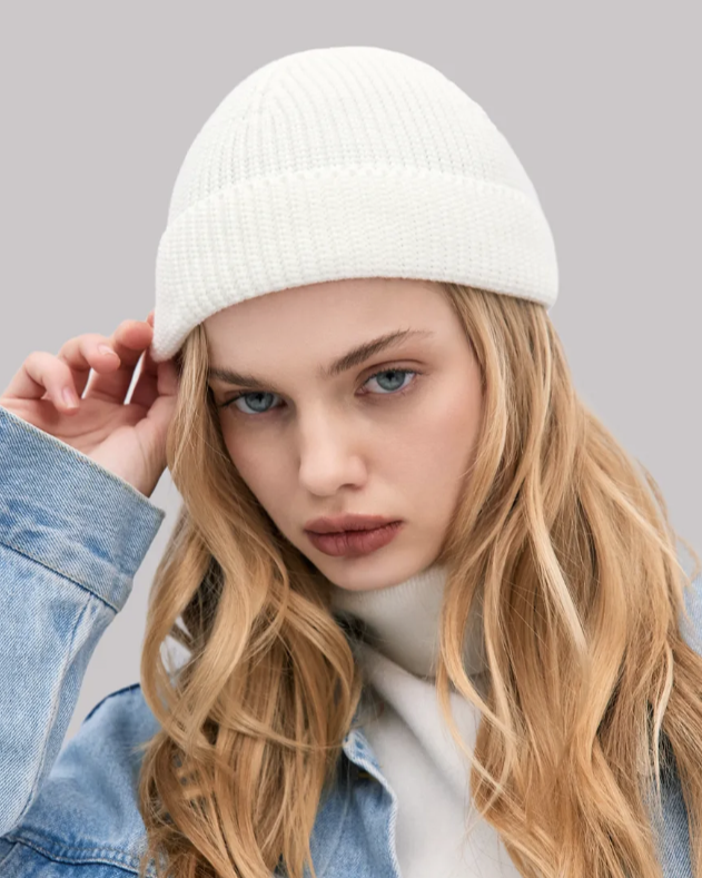 Woman wearing a white beanie and denim jacket on a gray background