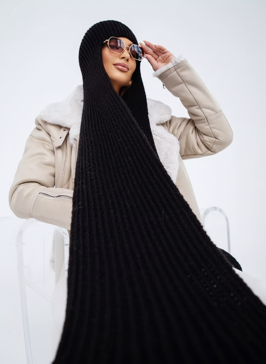 Person wearing a long black scarf, beige coat, and sunglasses on a white background