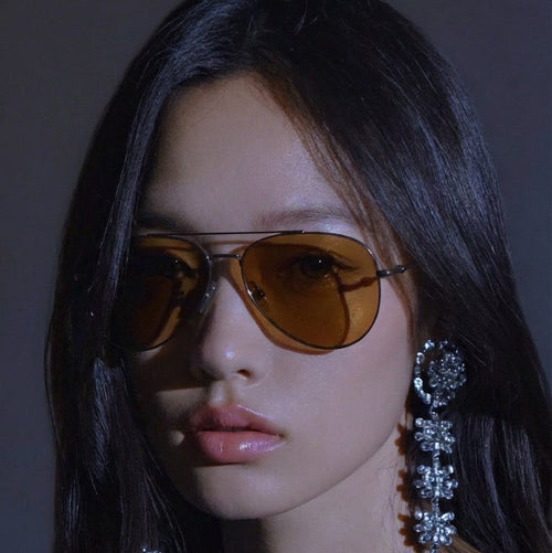 Woman wearing sunglasses with a red rose held close to her chest against a dark background