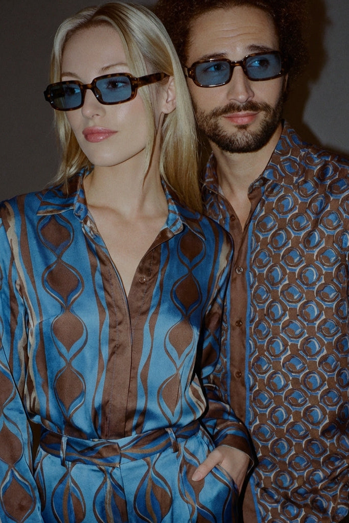Two people wearing patterned clothing and sunglasses against a dark background