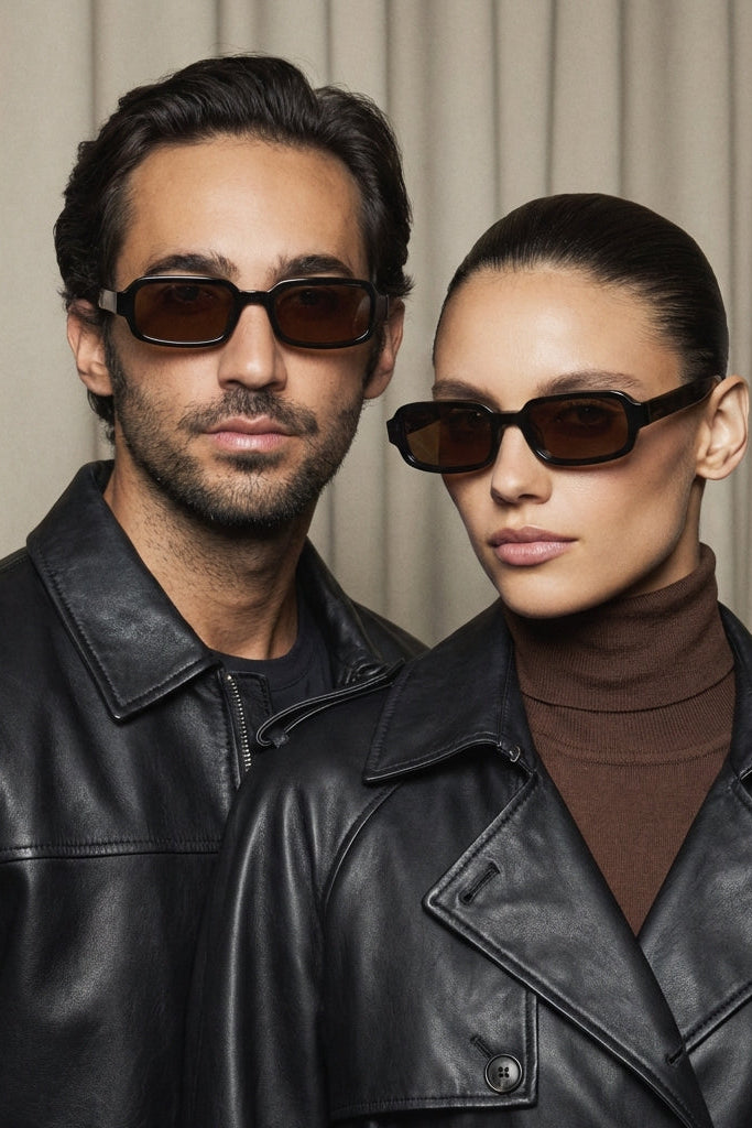 Two people wearing sunglasses and black leather jackets against a neutral background