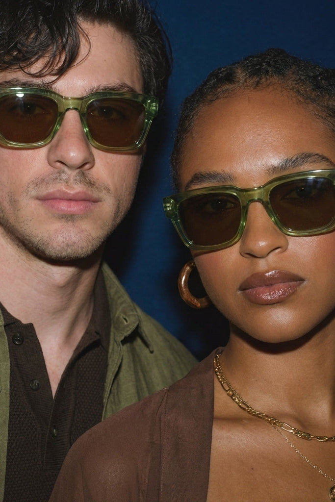Two people wearing green sunglasses against a blue background
