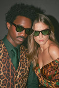 Two people wearing sunglasses and leopard print clothing against a dark background